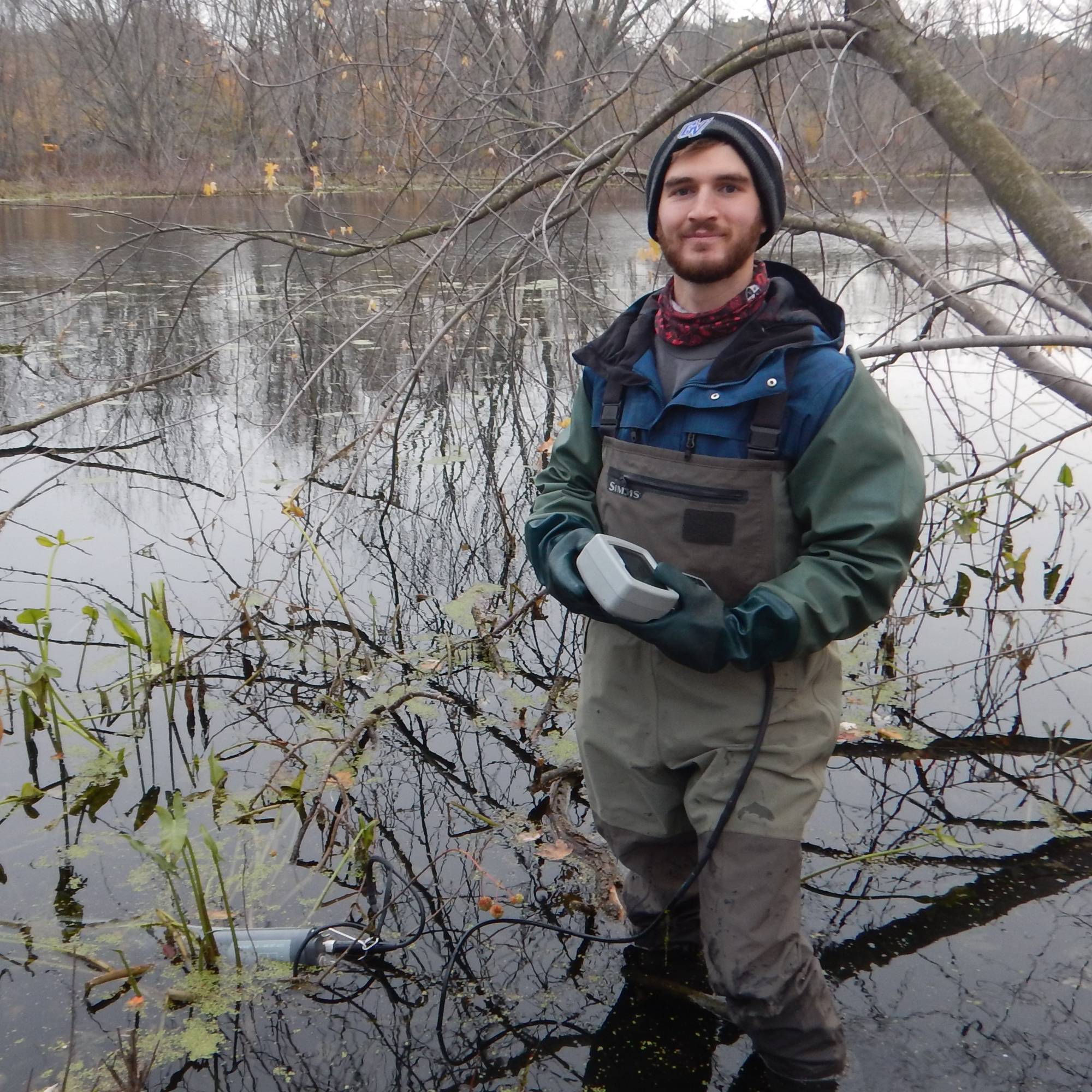 A student is standing in a wetland at riverside park holding a YSI.